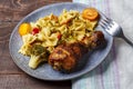 Pasta with vegetables and cherry tomatoes next to a baked chicken leg on the table next to a light napkin and a fork. Royalty Free Stock Photo
