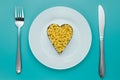 Pasta on a white plate with fork and knife on turquoise background. Heap of uncooked macaroni. Shape of heart, symbol of love. Cre Royalty Free Stock Photo