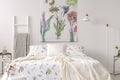 A pastel bedroom interior with a bed dressed in green plants pattern white linen. Fabric painted in flowers and birds on the backg