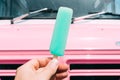 Pastel blue ice cream with a pink ice cream truck or van in the background. Hand holding ice cream.