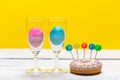 Happy Easter - pastel blue and pink egg in a glass of champagne on a bright, spring background next to a colorful donut with the w