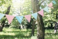 Pastel bunting flags hanging among trees. Summer garden party. Outdoor birthday, wedding decoration. Midsummer, festa Royalty Free Stock Photo