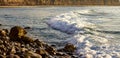 Pastel colored foam rolling infront of wave towards rocky shore with cliff and sandy beach Royalty Free Stock Photo