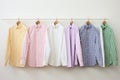 Pastel-colored shirts hanging on hangers against white wall in a minimalist setting