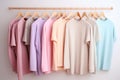 Pastel-colored t-shirts and sweatshirts hanging on hangers against white wall in minimalist setting
