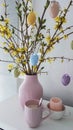 Pastel colored vase with forsythia and easter eggs and a pink cup of coffee Royalty Free Stock Photo