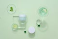 Pastel green background with cosmetic mockup jar decorated with slices cucumber and glassware.