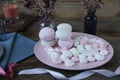 Pastel marshmallow flowers on a pink plate on a rustic wooden background with spring flowers