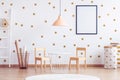 Pastel orange lamp above small white industrial table with wooden chairs in kid`s room