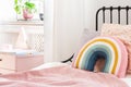 Pastel pillows on pink bed in girl`s rainbow bedroom interior with white cabinet.