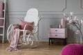 Pastel pink blanket and pillow on white rocking chair in sophisticated room with nightstand and flowers in glass vase, copy space