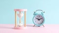 Pastel pink hourglass and teal alarm clock sit side-by-side on a Royalty Free Stock Photo