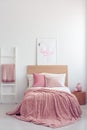 Pastel pink pillow and blanket on single wooden bed with white bedding in scandinavian bedroom interior