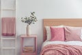 Pastel pink pillow and blanket on single wooden bed with white bedding in scandinavian bedroom interior Royalty Free Stock Photo