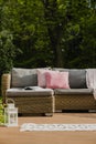 Pastel pillows on grey sofa in green garden with wooden terrace