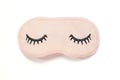 Pastel pink sleep mask with closed eyes embroidered on it with eyelashes on white background. Top view, flat lay.
