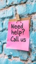 Pastel Pink Sticky Note with Need Help Call Us on a Textured Blue Wall, Offering Support and Help Royalty Free Stock Photo