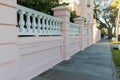 Pastel-pink wall with small white columns on sidewalk