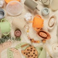 Pastel silicone collection of tableware, cutlery, bibs, accessories and wooden toys for children on cloth background.