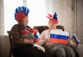 Pastimes. An elderly women supports sport team sitting against TV on the backgrond of shining window