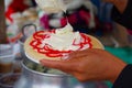 PASTO, COLOMBIA - JULY 3, 2016: woman adding some cream to a wafer with strawberry syrup and coconut