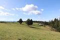 pastoral summer landscape with a green mountain meadow, a wooden cabin in the distance and a blue sky with harmless white clouds Royalty Free Stock Photo