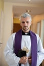 During a pastoral visit, a handsome young priest holds an envelope with money in the Holy Bible. Royalty Free Stock Photo