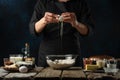 Pastry chef breaks egg into glass bowl. Backstage of cooking waffle on rustic wooden table with ingredients on dark blue Royalty Free Stock Photo