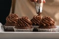 Pastry chef decorates cupcakes with chocolate cream from pastry bag. Homemade cocoa muffins close up