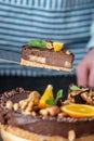 Pastry chef in hand holding a piece of chocolate cake with orange and peanuts. Healthy raw desserts for vegan food Royalty Free Stock Photo