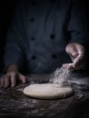 pastry chef hand sprinkling white flour over Raw Dough on kitchen table. Royalty Free Stock Photo