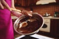 Pastry chef manufacturer of chocolate confectionery mixing melted chocolate mass in a steel bowl with a wooden spoon