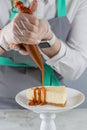 Pastry chef pours caramel on a slice of the freshest cheesecake on a white plate