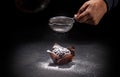 Pastry chef putting powdered sugar on delicious chocolate muffin on dark background
