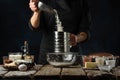 Pastry chef sifts flour into glass bowl. Backstage of cooking waffle on rustic wooden table with ingredients on dark blue Royalty Free Stock Photo