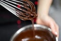 Pastry chef whips melted chocolate in a bowl with a metal wire whisk close up. Royalty Free Stock Photo