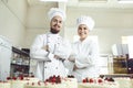 Pastry chefs in white uniform are smiling at bakery.