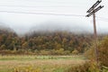 Pasture in autumn mountains with power pole. Valley of the Carpathian mountains in morning fog. Meadow with power lines and wire