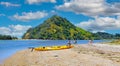 Beautiful sand beach with canoe, people relaxing in sun, water bay, lush green hill, blue sky fluffy cumulus clouds