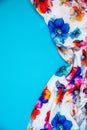 A patch of white fabric with multicolored flowers with drapery on a bright blue background. Space for text Royalty Free Stock Photo