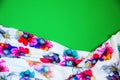 A patch of white fabric with multicolored flowers with drapery on a bright green background. Space for text