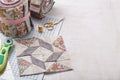 Patchwork block on craft mat, rolls of fabric, sewing accessories on white wooden surface