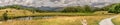 A path leading through a field towards a forest and mountains. Royalty Free Stock Photo