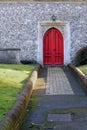 Path leading to a red wooden door into an old stone church build Royalty Free Stock Photo