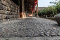 A path from a natural stone of a cobble-stone. Stone wall, wooden poles, outdoor building under the open sky. Royalty Free Stock Photo