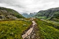 Path over green pasture in the mountains of Western Norway with snow on the summits and a dark cloudy sky Royalty Free Stock Photo