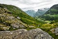 Path over green pasture in the mountains of Western Norway with snow on the summits and a dark cloudy sky Royalty Free Stock Photo