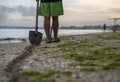 Path of a shovel behind a man searching for a precious metal using a metal detector on beach at sunset time