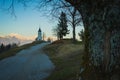 Path towards cute  fantastic charming Saint Primoz church on a small hill with mountains in background at sunset, Jamnik village, Royalty Free Stock Photo