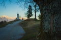 Path towards cute  fantastic charming Saint Primoz church on a small hill with mountains in background at sunset, Jamnik village, Royalty Free Stock Photo